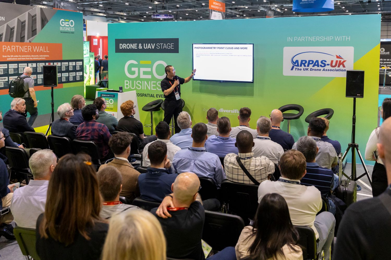 Man speaking at GEO Business to a busy crowd